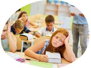 Children in a classroom appearing bored and tired, with books open on desks. A teacher stands in the background holding papers.