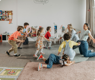 Children and two adults play joyfully in a playroom. Kids wear colorful clothes, and a speech bubble on the wall reads, "I am not young enough to know everything."