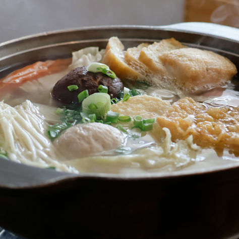 Steaming pot of chanko nabe with chicken, tofu, mushrooms, napa cabbage, carrots and greens in a light broth