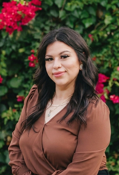 Poised before a lush backdrop, Yessenia is framed by deep greens and fuchsia clusters.