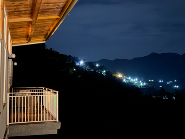 Nighttime balcony view overlooking a dark valley with distant village lights.