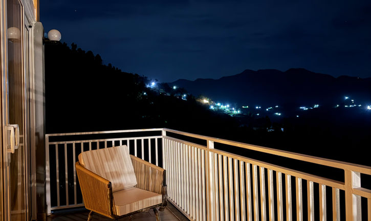 Cozy balcony chairs and table overlooking mountain village lights at night.