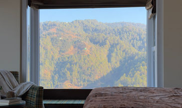 Cozy bedroom with a large bay window with seating overlooking a scenic mountain landscape.