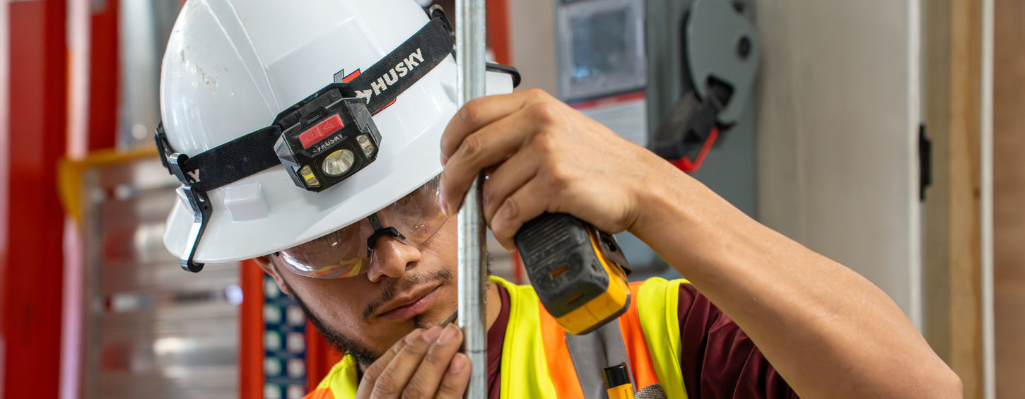 An electrical apprentice at Hays Electrical Services marking measurements on a piece of conduit