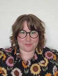 Rosie is a white woman in her mid 20's, she has short brown wavy hair and is wearing glasses and a button up collared shirt with sunflowers on it.