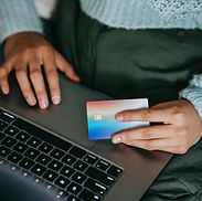 A person with a credit card in hand and a computer on their lap