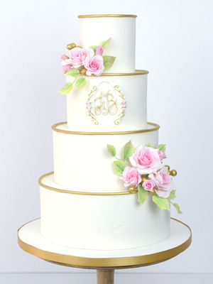 Classic 4-tier white wedding cake with pink sugar roses, green foliage and gold accents which frame a custom sugar monogram.