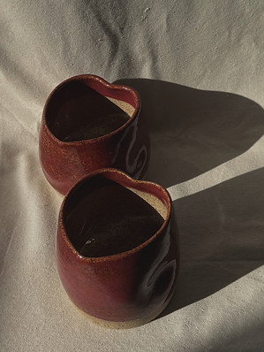 Two heart shaped wheel thrown ceramic mugs in an earthy red glaze