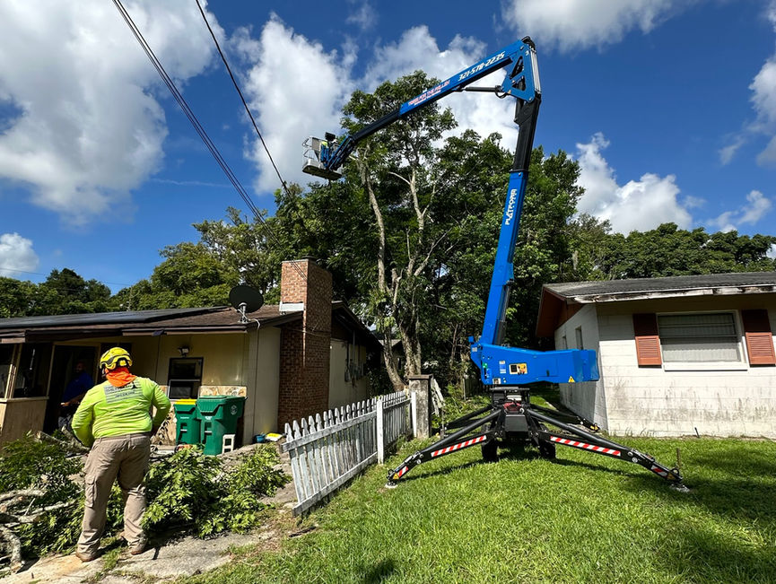 A crew member in a green shirt standing beside the outriggers of a blue boom lift in New Smyrna Beach, Florida.