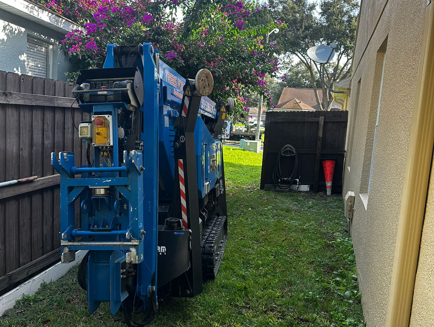 A blue chipper parked in a narrow side yard with flowering bushes behind it in New Smyrna Beach, Florida.