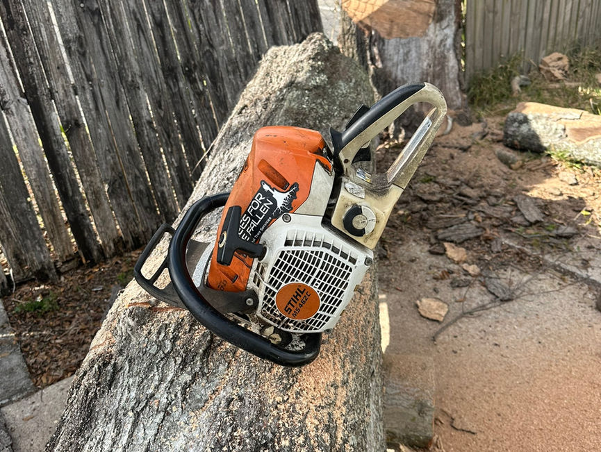 A Stihl chainsaw resting on a cut oak log, with a fresh stump and a wooden fence behind it in Edgewater, Florida.