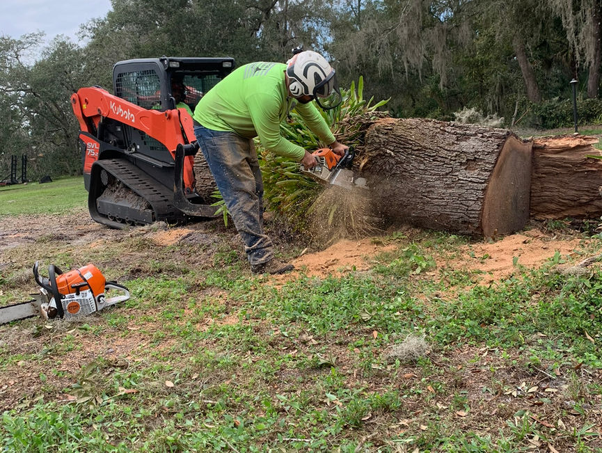 A crew member guiding a large log while an orange loader holds it.