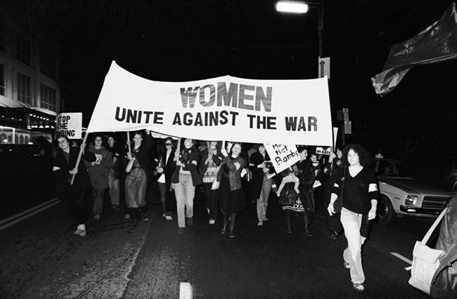 women holding a banner that says women unite against the war