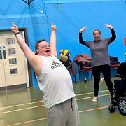 A male service user celebrating a victory during a game of basketball. A Lotus team member can be seen in the background, cheering him on.
