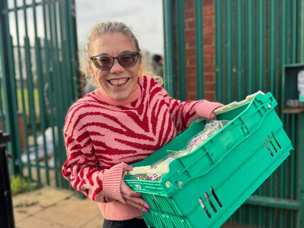 A cheerful volunteer from Lotus, helping out at The Bread and Butter Thing initiative, carries a basket full of fresh produce into Waterside Community Centre.
