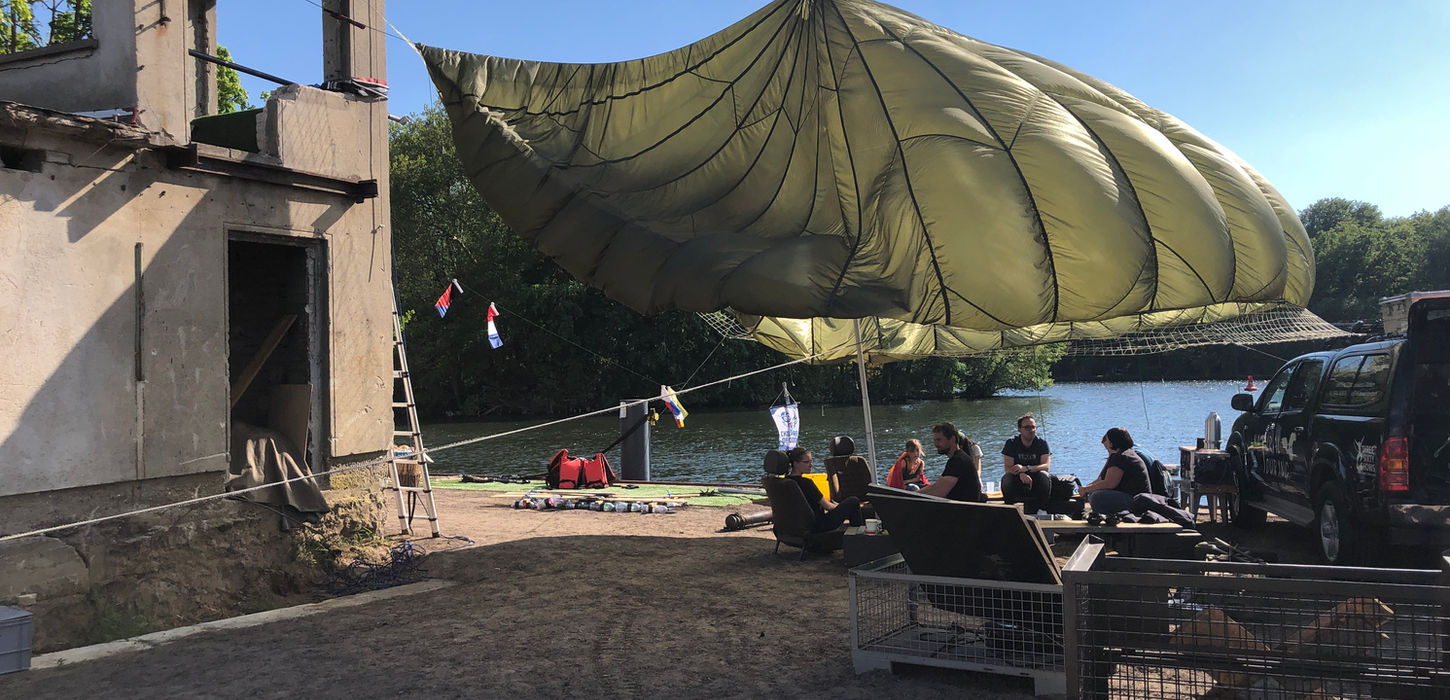 Großes militärgrünes Zelt oder Überdachung im Freien vor blauem Himmel, mit technischer Ausrüstung im Vordergrund