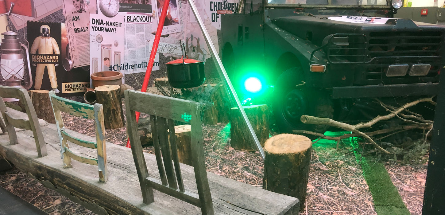 Indoor-Ausstellungsbereich mit grüner Beleuchtung, verschiedenen Displays und Informationstafeln in einem atmosphärisch gestalteten Raum