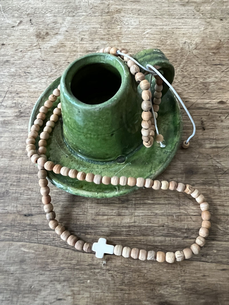 Bracelet Triple tour en perles de bois posé sur une tasse verte, sur bois rustique.