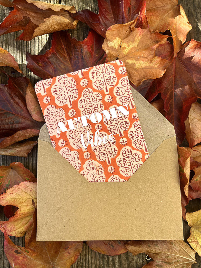 Carte orange avec motif arbres et texte ATON, dans une enveloppe contre feuilles.