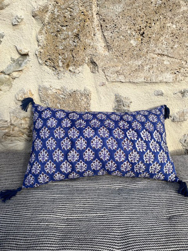 Coussin bleu orné d'un motif floral et de pompons dans un cadre rustique.