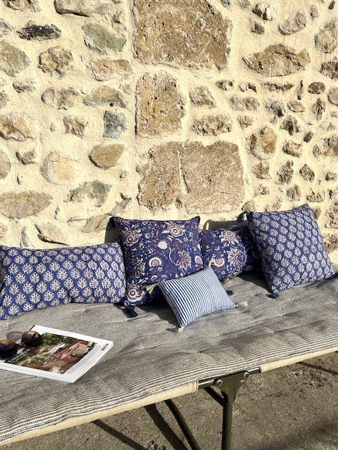 Coussins bleus sur une banquette en bois devant un mur en pierres apparentes.
