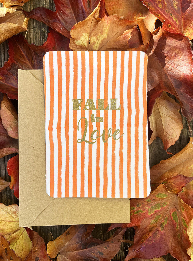 Carte postale avec Fall in Love sur fond orange et blanc, enveloppe marron.