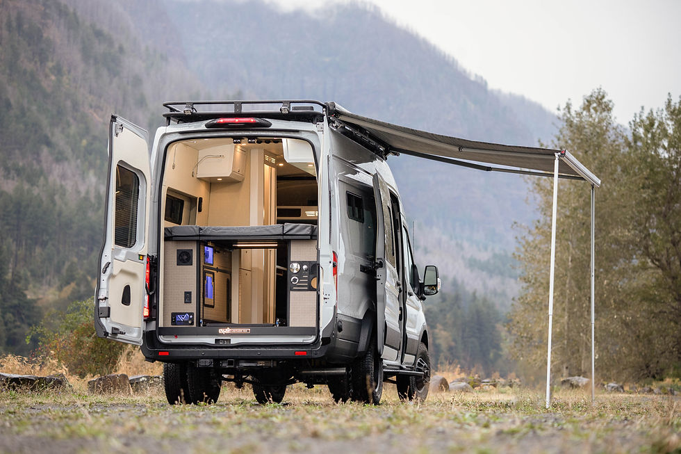 Ford Transit Camper Van Conversion with rear doors open showing a bed with wheel well cabinets underneath. The van is parked in a scenic setting with tree filled hills in the background.