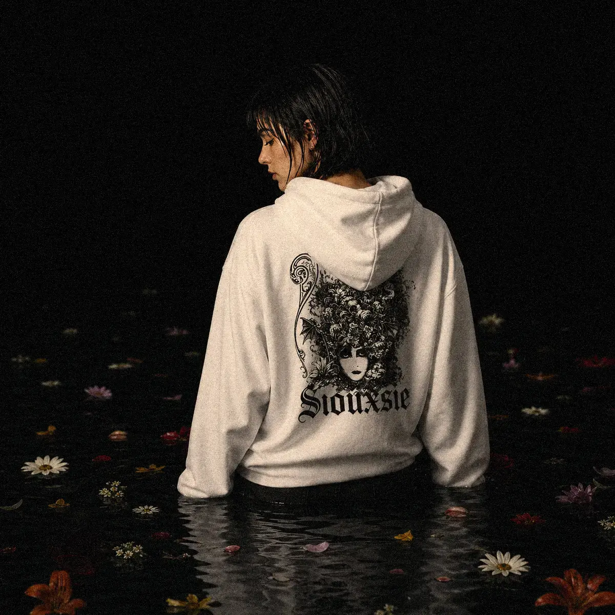 Mulher usando moletom branco com capuz e estampa Siouxie and the Banshees em preto dentro de lago, com flores