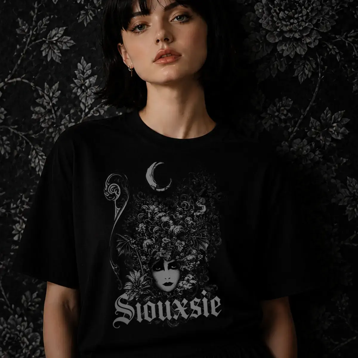 Menina de camiseta preta com estampa Siouxsie apoiada na parede com papel de parede de flores