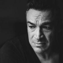 Actor Aleks Paunovic in a dramatic black-and-white portrait by Nick Holmes, with a serious expression and soft shadow lighting.