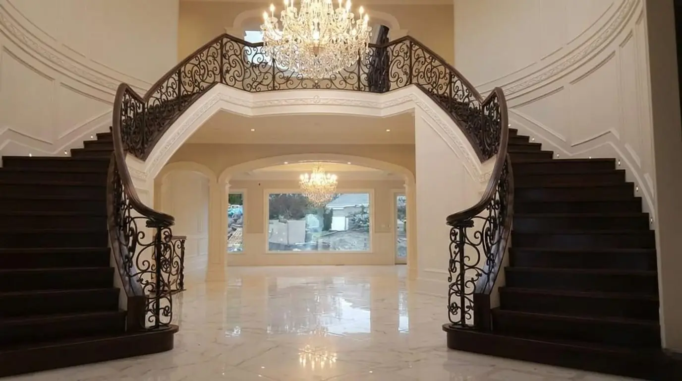Split (Curved) Staircase featuring custom metal stair railings, ornate wrought iron interior staircase railings, dark wood treads, and a chandelier in a luxury entryway.