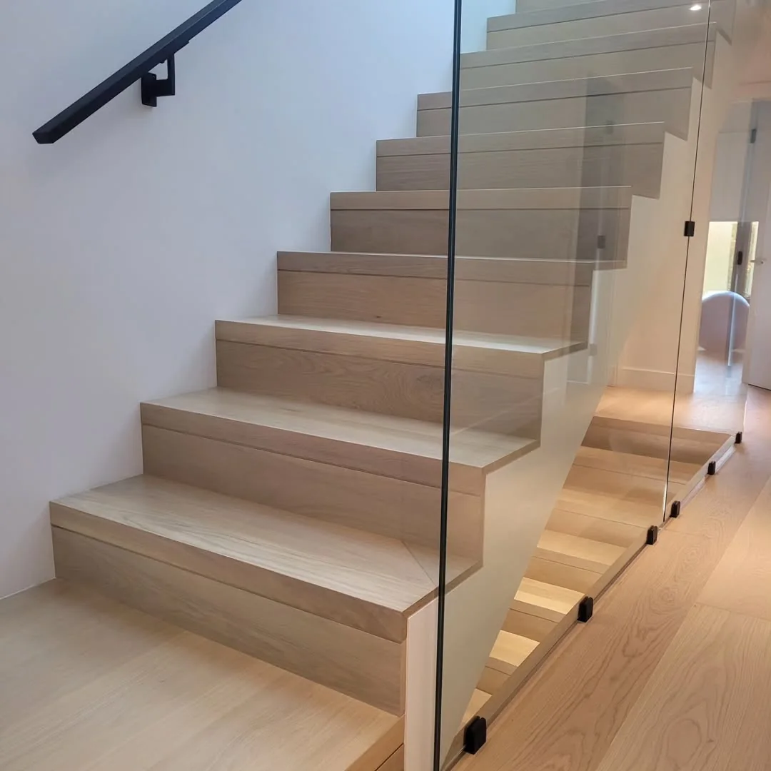 Custom interior stairs with wide oak treads and clear glass guardrail in a contemporary home