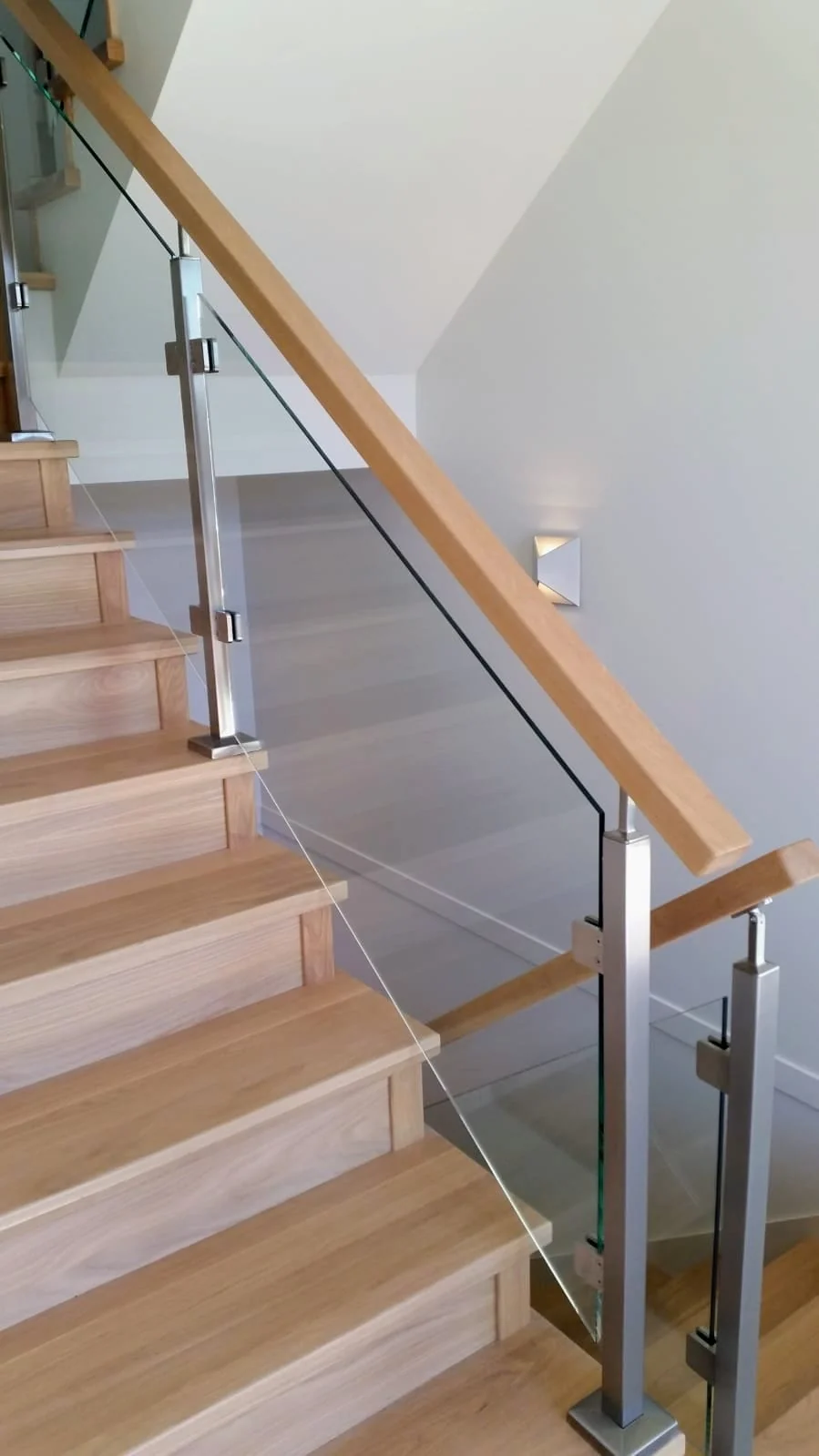 Floating-style wood stairs with glass panel railing, stainless steel posts and oak handrail in contemporary Vancouver area home by Classic Railings.