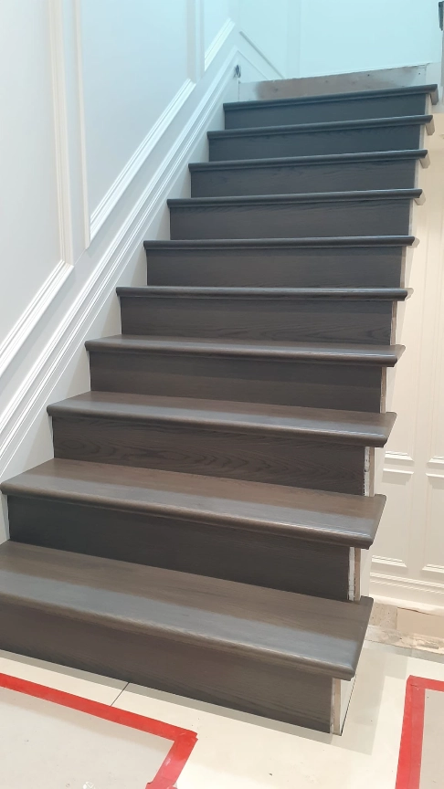 Custom interior staircase with dark-stained wood treads and rounded nosings against a white paneled wall, showing stair nosing detail.