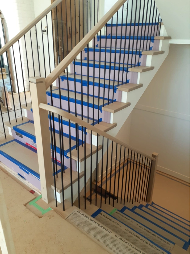 Interior U-shaped staircase under construction with temporary blue tread protection and a light wood railing with slim black balusters