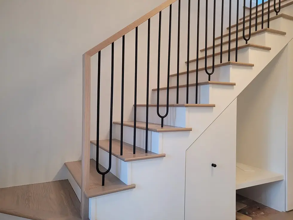 Modern interior stair railing with black metal balusters and wood handrail on light wood treads and white stringers.