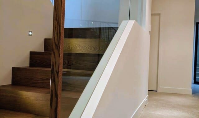 Modern interior staircase with dark wood treads, glass panel railing, and wood handrail in a clean white hallway in Port Coquitlam home.