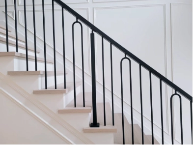 Interior wood stair with black metal handrail and balusters showing a continuous graspable railing along the flight