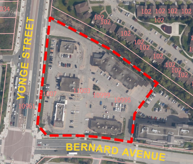Aerial view of a parking lot and buildings outlined in red near Yonge Street and Bernard Avenue. Streets labeled in yellow, numbers in red.