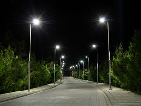 Lit pathway at night, flanked by trees and illuminated by bright streetlights. The scene has a serene, quiet ambiance.
