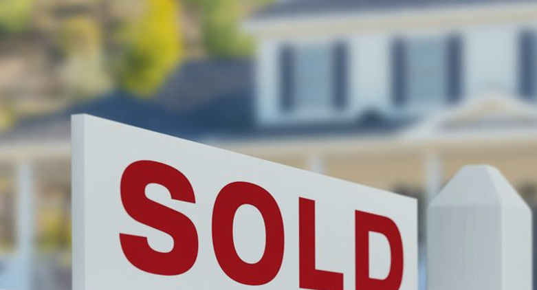 white home with grey roof trees in background and a white for sale with red text in front