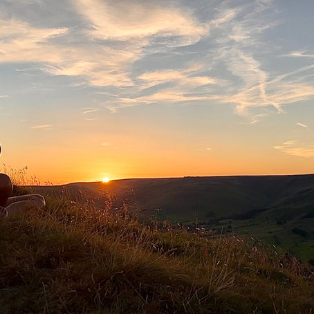 Woman sitting in a yoga pose with eyes closed on the edge of Mam Tor in the Peak District, embracing stillness and sunset calm under a clear evening sky – a mindful moment of relaxation, peace, and connection with nature.