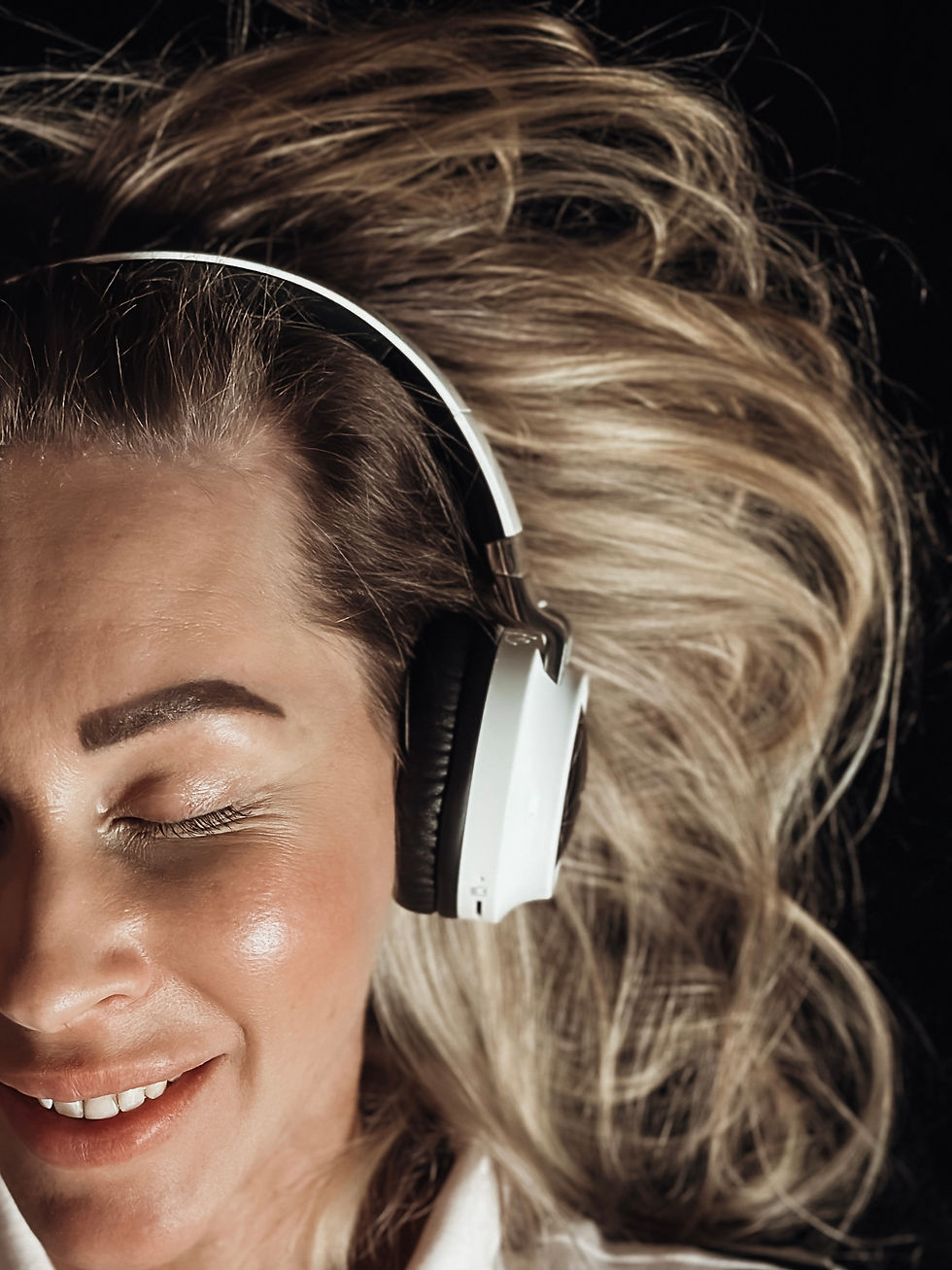 A smiling portrait of a person wearing big earphones and a striped polo shirt, listening to music, with a relaxed and happy expression.