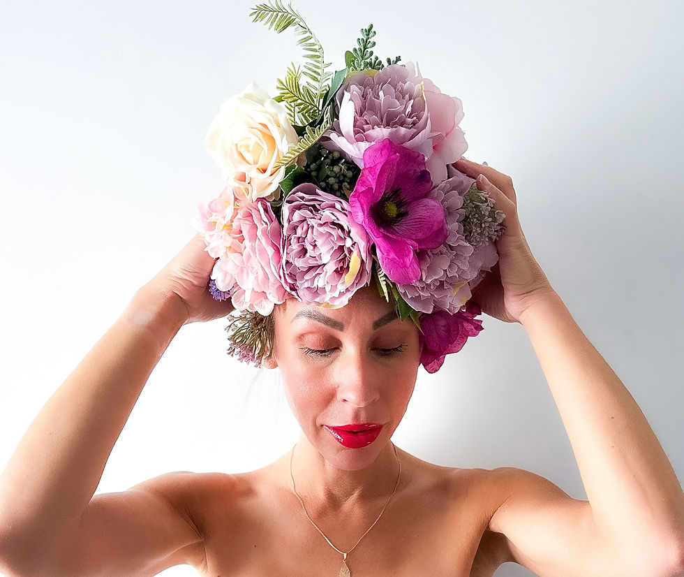 Portrait of a woman smiling warmly, with vibrant flower decorations in her hair, radiating positivity and joy. The floral arrangement adds a playful, natural touch, complementing her cheerful expression and bright, inviting demeanor
