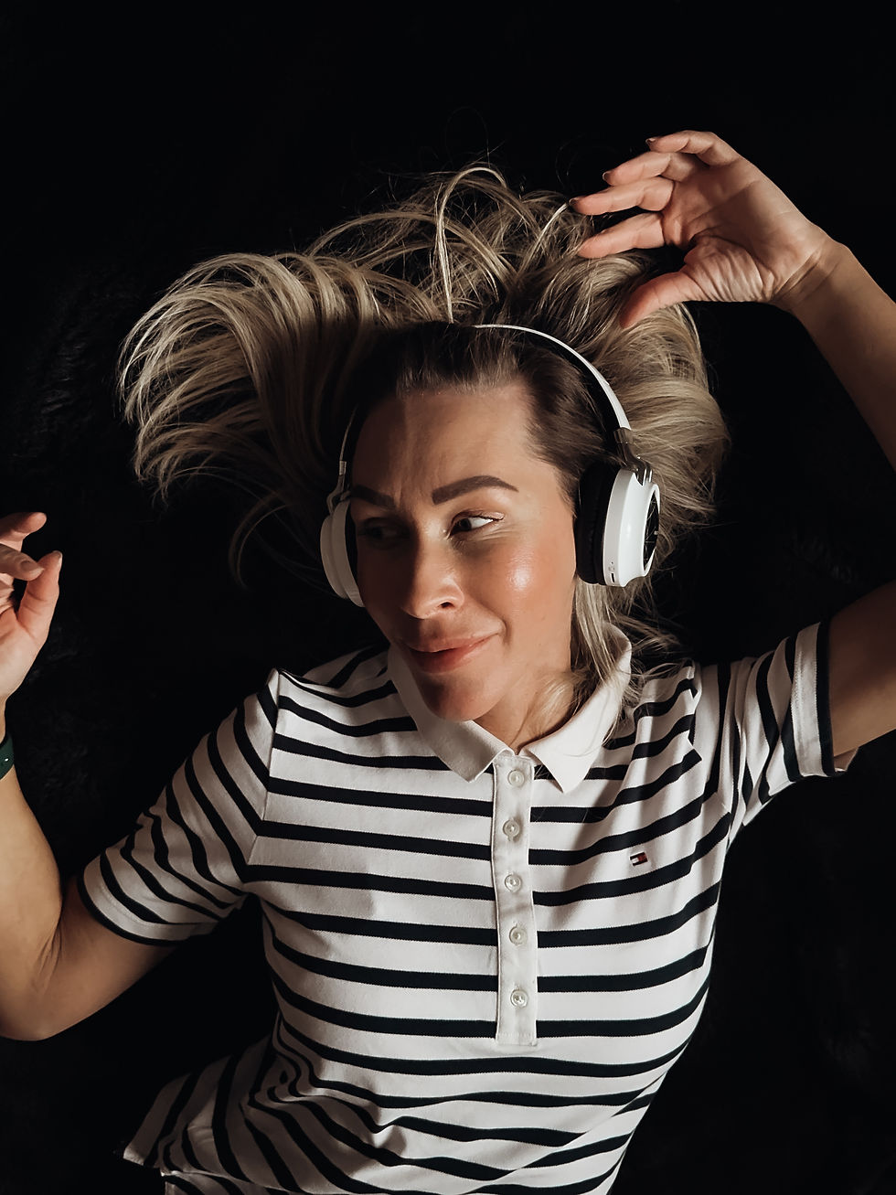 A smiling portrait of a person wearing big earphones and a striped polo shirt, listening to music, with a relaxed and happy expression.