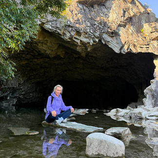 Woman sitting in a yoga pose on a stepping stone in Rydal Cave, Lake District, with the mountain view framing the cave entrance — a serene moment of mindfulness and balance.