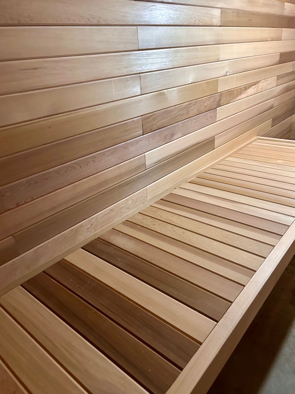 Custom cedar sauna bench with horizontal wall paneling and natural wood grain detail.