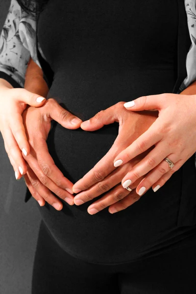 A pregnant woman belly and her partner with their hands on her belly