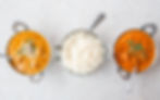 Three ornate bowls sit on a speckled table: two with orange curry garnished with herbs and nuts, and one with steamed white rice.