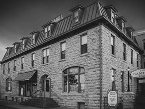 Stone building with arched windows and metal roof in black and white. A moody sky is overhead.